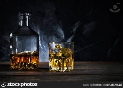 Decanter and glass of whiskey with ice on wooden table. Decanter and glass of whiskey with ice