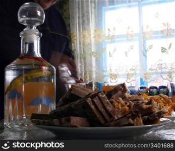 Decanter with vodka with pepper and meat on a plate against a window