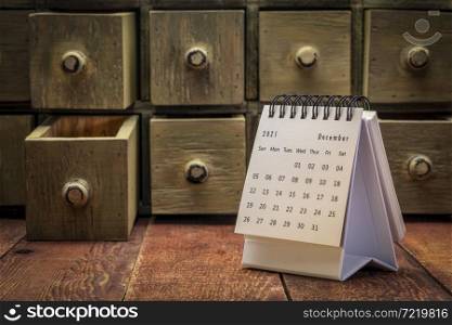 December 2021 - spiral desktop calendar on a weathered barn wood table with rustic apothecary drawers in background, time and business concept