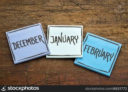 December, January and February - handwriting in black ink on sticky notes against rustic wood