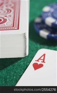 Deck of cards and poker chips on a poker table with ace of hearts showing (close up/selective focus)