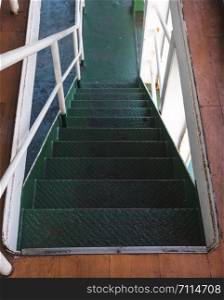 Deck of moored passenger transport ship on the embankment with white handrail to the cabins and green stairs
