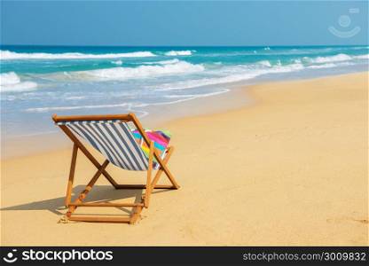 Deckchair with colorful bag on the beach near blue water side - vacation and travel concept.Striped deck chair on the sand.