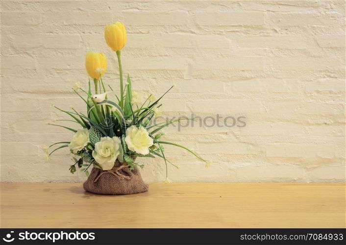 Decorated artificial flowers on wooden table with painted brick wall background