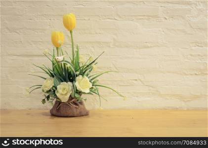 Decorated artificial flowers on wooden table with painted brick wall background