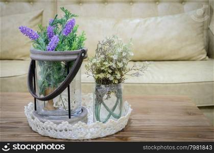 Decorated artificial flowers on wooden table with sofa background in living room