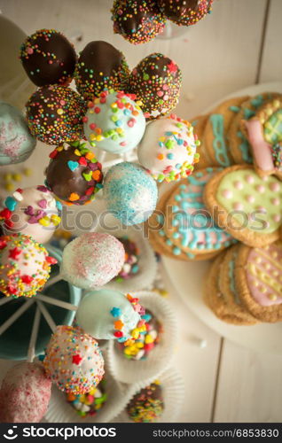 Decorated candies, cake pops and cookies on white wooden desk