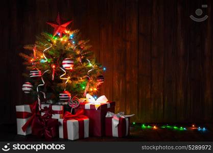 Decorated Christmas tree. Decorated Christmas tree with glowing lights and gift boxes on wooden background