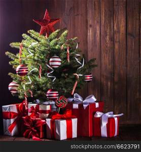 Decorated Christmas tree with candy canes , star , striped baubles and gift boxes on wooden background. Decorated Christmas tree
