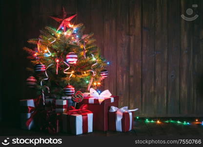 Decorated Christmas tree with glowing lights and gift boxes on wooden background. Decorated Christmas tree and gifts