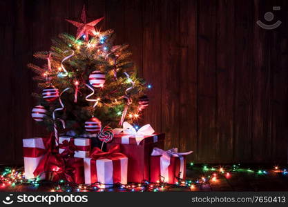 Decorated lighted Christmas tree and gift boxes on wooden background. Decorated Christmas tree