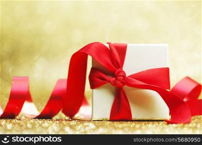 Decorated present in white box with red ribbon on golden background