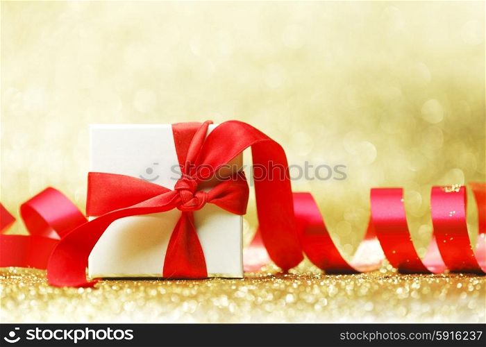 Decorated present in white box with red ribbon on golden background