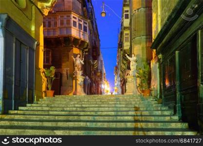 Decorated street in old town of Valletta, Malta. Narrow street stairs with corners of houses, decorated with statues of saints at night in the old town of Valletta, Malta