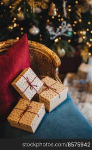Decorated wrapped present boxes on comfortable armchair near New Year tree. Christmas gifts prepared by unrecognizable person. Beautiful holiday decorated room. Celebration concept