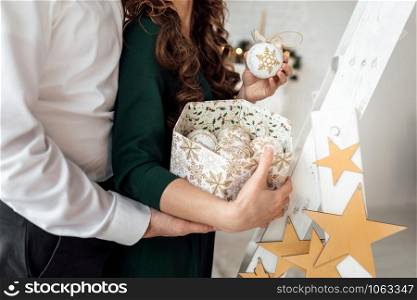 Decorating Christmas tree. Wife and husband holding a box with christmas toys in scandinavian style. Closeup photo of hands.