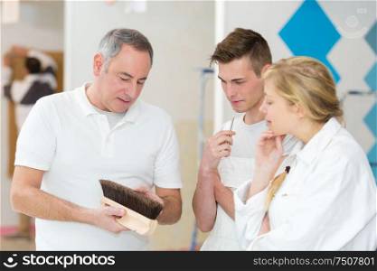 decorating students looking at wallpapering brush with teacher