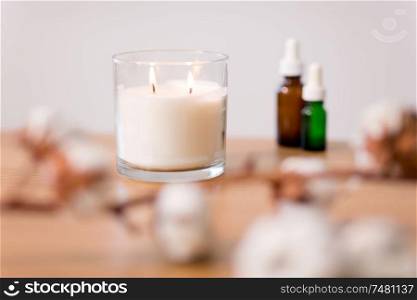 decoration and aromatherapy concept - burning white home fragrance candle in glass holder on table. burning home fragrance candle in glass holder