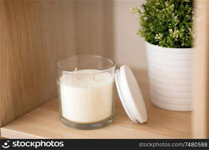decoration and interior concept - white fragrance candle in glass holder and pot flower on wooden shelving at home. fragrance candle in glass holder on shelving