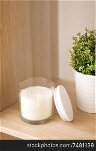 decoration and interior concept - white fragrance candle in glass holder and pot flower on wooden shelving at home. fragrance candle in glass holder on shelving