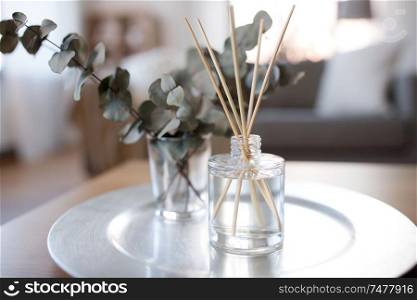 decoration, hygge and aromatherapy concept - aroma reed diffuser and branches of eucalyptus populus on table at home. aroma reed diffuser and branches of eucalyptus