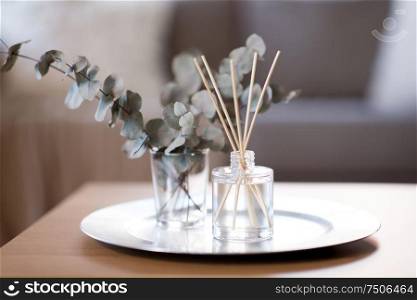 decoration, hygge and aromatherapy concept - aroma reed diffuser and branches of eucalyptus populus on table at home. aroma reed diffuser and branches of eucalyptus