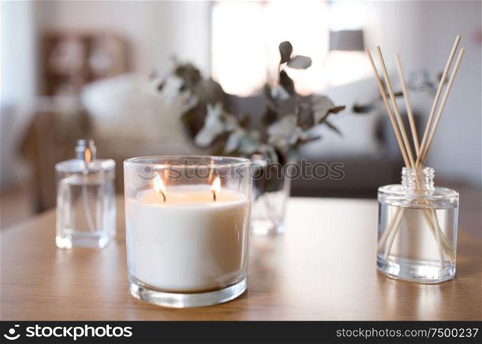 decoration, hygge and aromatherapy concept - aroma reed diffuser, burning candle and perfume on table at home. aroma reed diffuser, burning candle and perfume