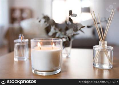 decoration, hygge and aromatherapy concept - aroma reed diffuser, burning candle and perfume on table at home. aroma reed diffuser, burning candle and perfume