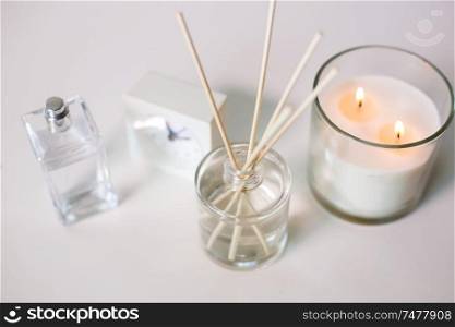 decoration, hygge and aromatherapy concept - aroma reed diffuser, burning candle and perfume on table. aroma reed diffuser, burning candle and perfume