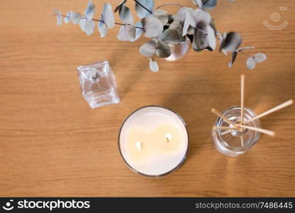 decoration, hygge and aromatherapy concept - aroma reed diffuser, burning candle, branches of eucalyptus populus and perfume on table. aroma reed diffuser, burning candle and perfume