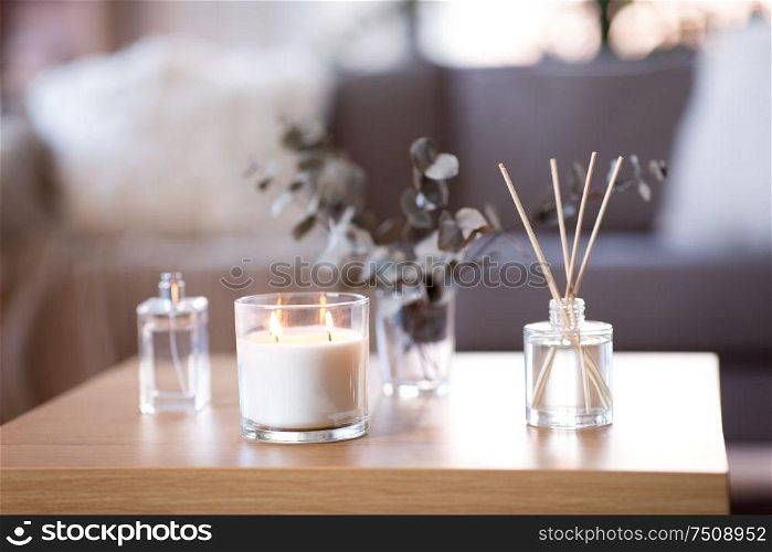 decoration, hygge and aromatherapy concept - aroma reed diffuser, burning candle, branches of eucalyptus populus and perfume on table at home. aroma reed diffuser, burning candle and perfume