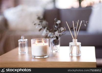 decoration, hygge and aromatherapy concept - aroma reed diffuser, burning candle, branches of eucalyptus populus and perfume on table at home. aroma reed diffuser, burning candle and perfume