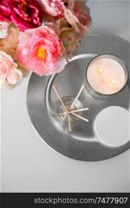 decoration, hygge and cosiness concept - aroma reed diffuser, burning candle and flower bunch on wooden table. aroma reed diffuser, candle and flowers on table