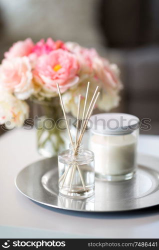 decoration, hygge and cosiness concept - aroma reed diffuser, candle and flower bunch on wooden table. aroma reed diffuser, candle and flowers on table