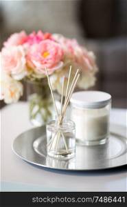 decoration, hygge and cosiness concept - aroma reed diffuser, candle and flower bunch on wooden table. aroma reed diffuser, candle and flowers on table