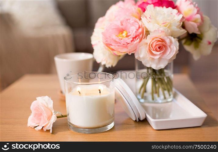 decoration, hygge and cosiness concept - burning fragrance candle and flower bunch in vase on wooden table. burning candle and flower bunch on table at home
