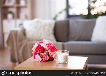 decoration, hygge and cosiness concept - burning fragrance candle and flower bunch at cozy home. burning fragrance candle and flower bunch at home