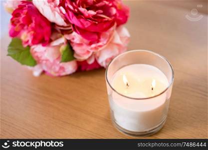 decoration, hygge and cosiness concept - burning fragrance candle and flower bunch on wooden table. burning fragrance candle and flower bunch on table