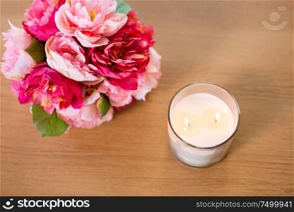 decoration, hygge and cosiness concept - burning fragrance candle and flower bunch on wooden table. burning fragrance candle and flower bunch on table