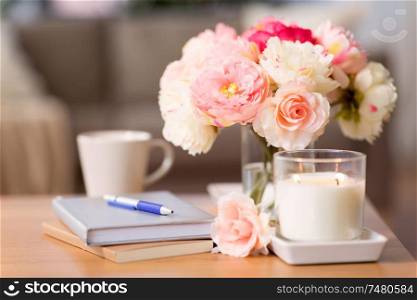 decoration, hygge and cosiness concept - burning fragrance candle, flower bunch, books and pen on wooden table. burning candle and flower bunch on wooden table