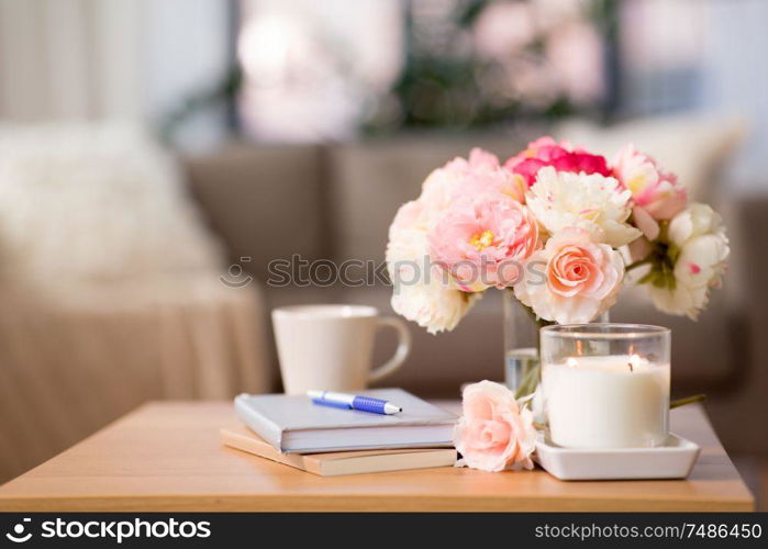 decoration, hygge and cosiness concept - burning fragrance candle, flower bunch, books and pen on wooden table. burning candle and flower bunch on wooden table