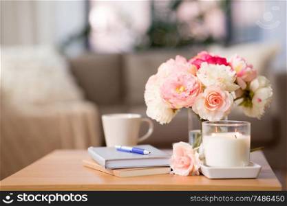 decoration, hygge and cosiness concept - burning fragrance candle, flower bunch, books and pen on wooden table. burning candle and flower bunch on wooden table