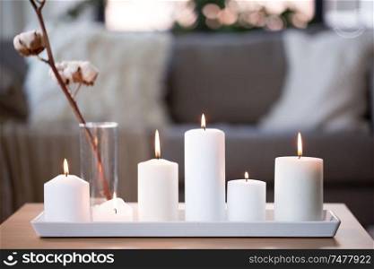 decoration, hygge and cosiness concept - burning white candles and cotton flower branch on table at cozy home. burning white candles on table at cozy home