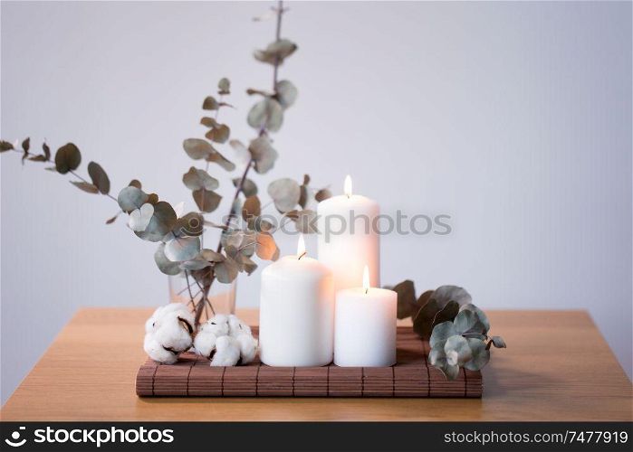 decoration, hygge and cosiness concept - burning white candles, branches of eucalyptus populus and cotton flowers on table. candles and branches of eucalyptus on table
