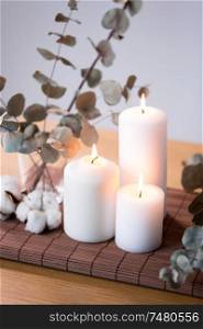 decoration, hygge and cosiness concept - burning white candles, branches of eucalyptus populus and cotton flowers on table. candles and branches of eucalyptus on table