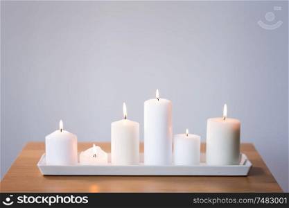 decoration, hygge and cosiness concept - burning white candles on tray on table. burning white candles on tray on table