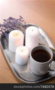decoration, hygge and cosiness concept - burning white candles, tea in mug and lavender flowers on tray on table. candles, tea in mug and lavender flowers on table