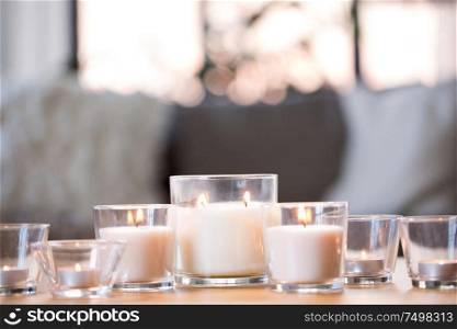 decoration, hygge and cosiness concept - burning white fragrance candles on table at home. burning white fragrance candles on table at home