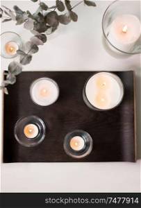 decoration, hygge and cosiness concept - burning white fragrance candles on tray and branches of eucalyptus populus on table. candles and branches of eucalyptus on table