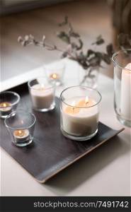 decoration, hygge and cosiness concept - burning white fragrance candles on tray on table at cozy home. burning fragrance candles on table at cozy home